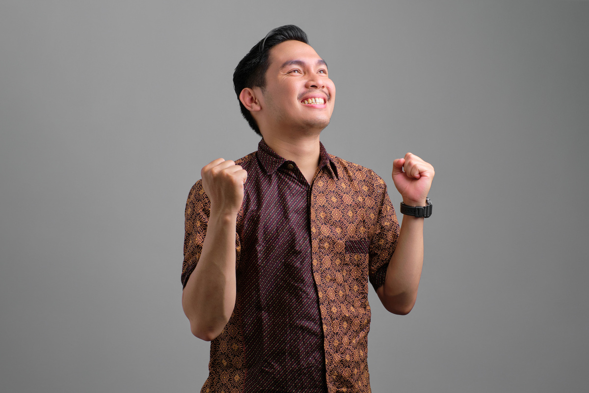 Excited young Asian man wearing batik shirt celebrating victory